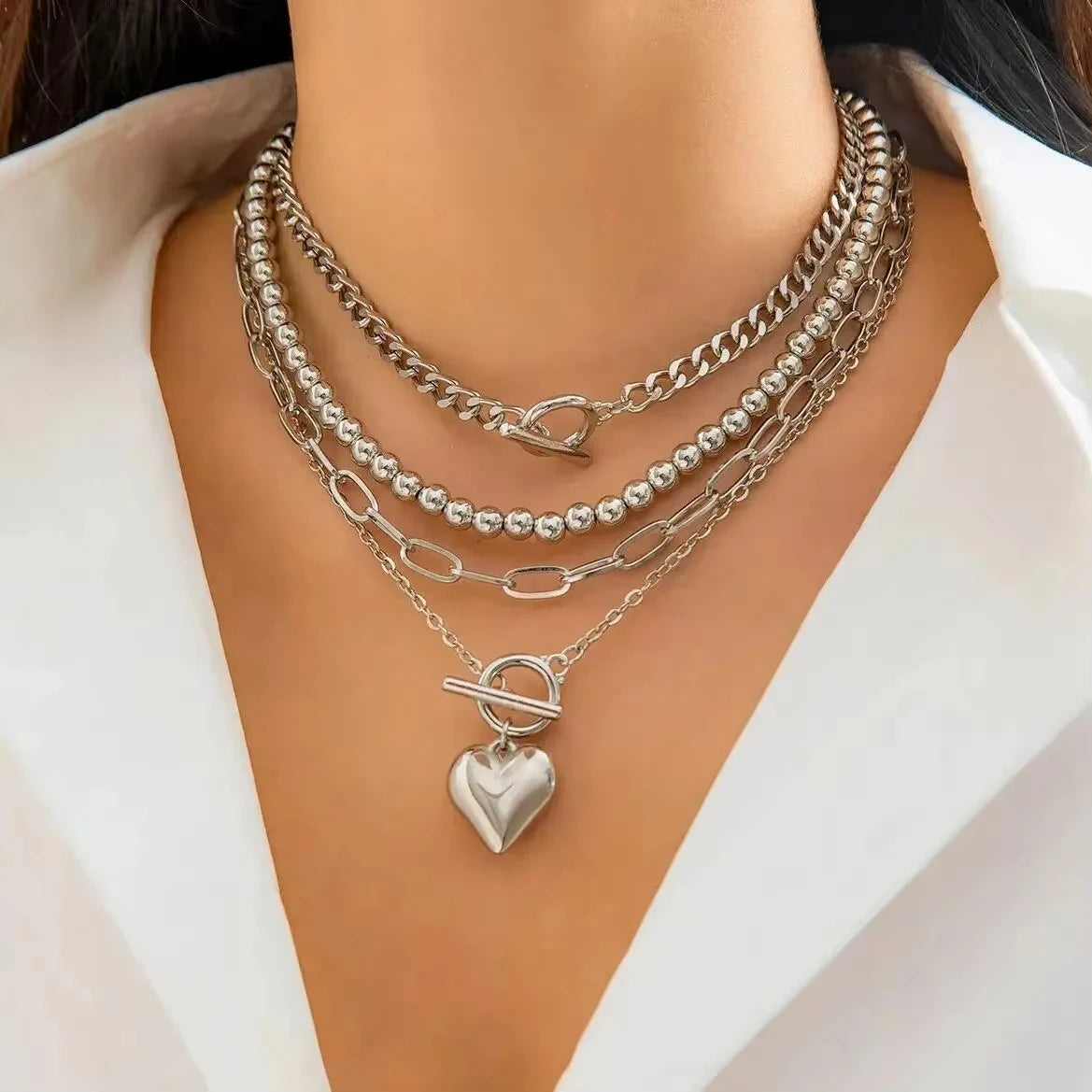 Stack of silver necklaces with a heart pendant on a white background