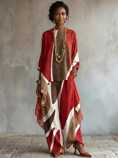 A woman models a matching two-piece outfit featuring a rust red, brown, and cream abstract patterned top and wide-leg trousers, styled with layered wooden bead necklaces and brown heels against a textured gray wall.