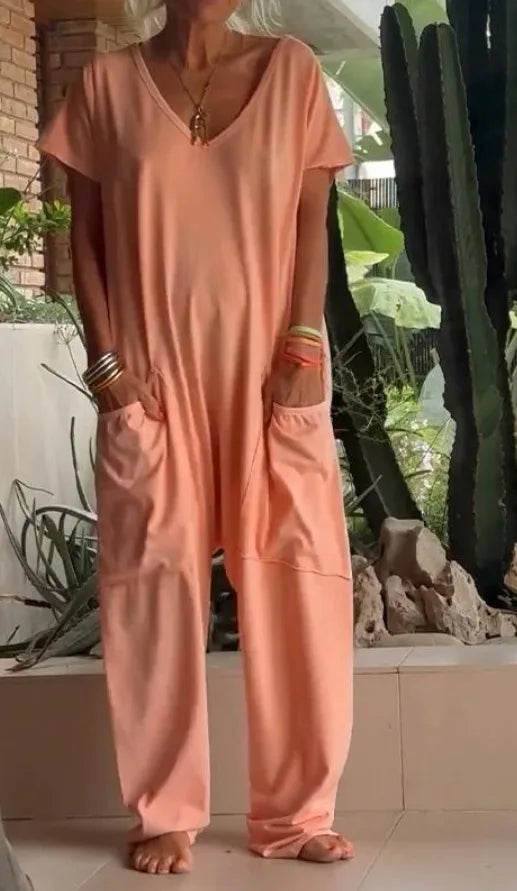Person wearing a peach-colored jumpsuit standing outdoors with plants and rocks in the background