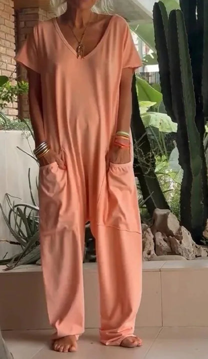 Person wearing a peach-colored jumpsuit standing outdoors with plants and rocks in the background