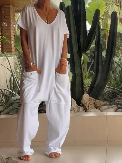 Person wearing a loose-fitting white outfit standing in a garden with plants and stones.