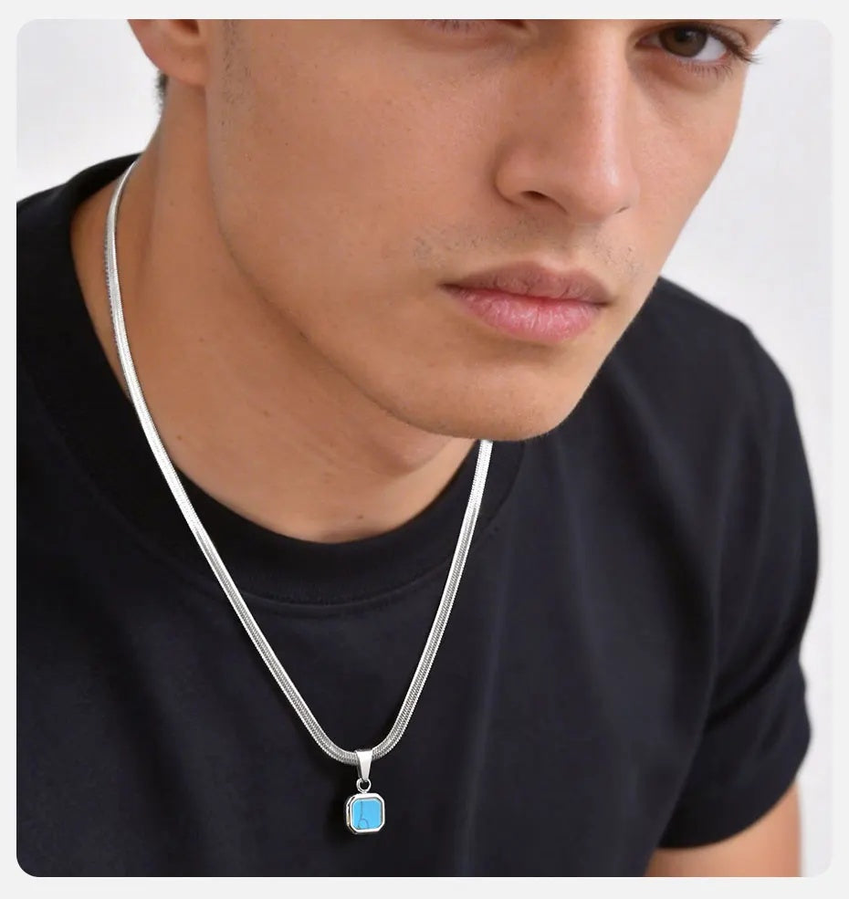 Close-up of a person wearing a black shirt with a silver necklace featuring a blue pendant.