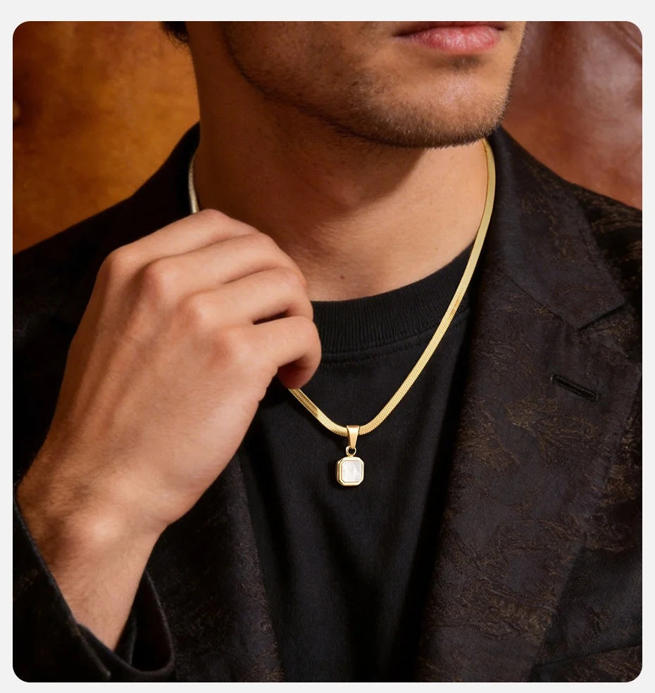 Man adjusting a gold necklace with a pendant against a blurred background