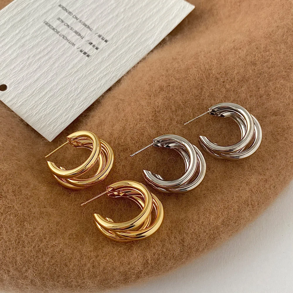 Pair of gold and silver hoop earrings on a brown surface with a white card.