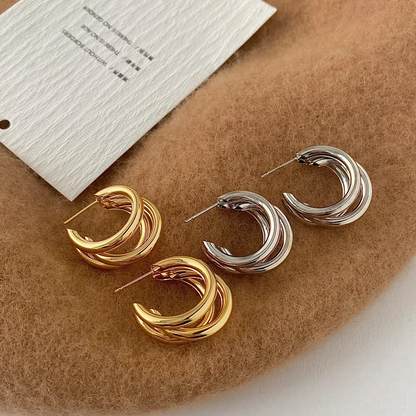 Pair of gold and silver hoop earrings on a brown surface with a white card.