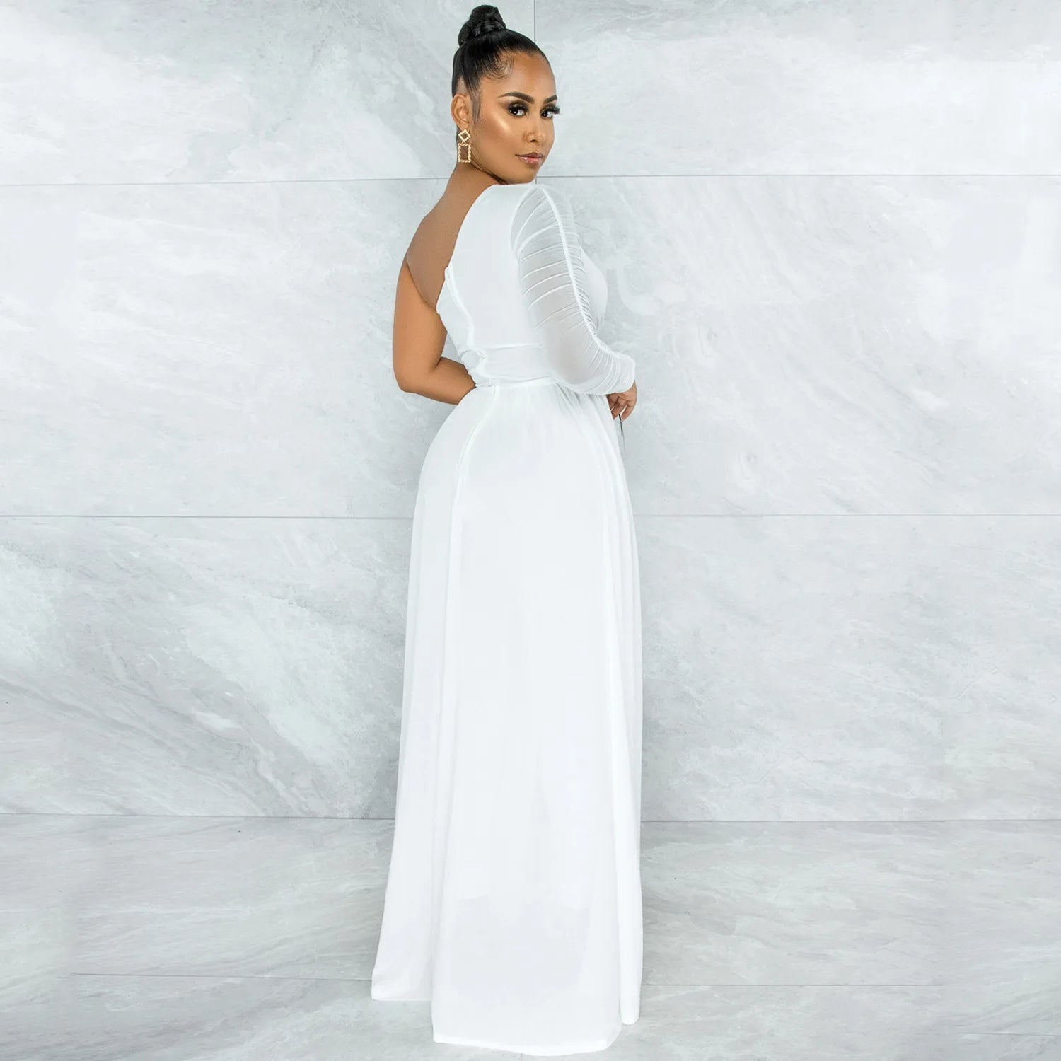 A stylish white jumpsuit with a sheer sleeve, cinched belt, and flowing train viewed from the back. The outfit is paired with gold accessories, and the background features a contemporary gray marble texture.