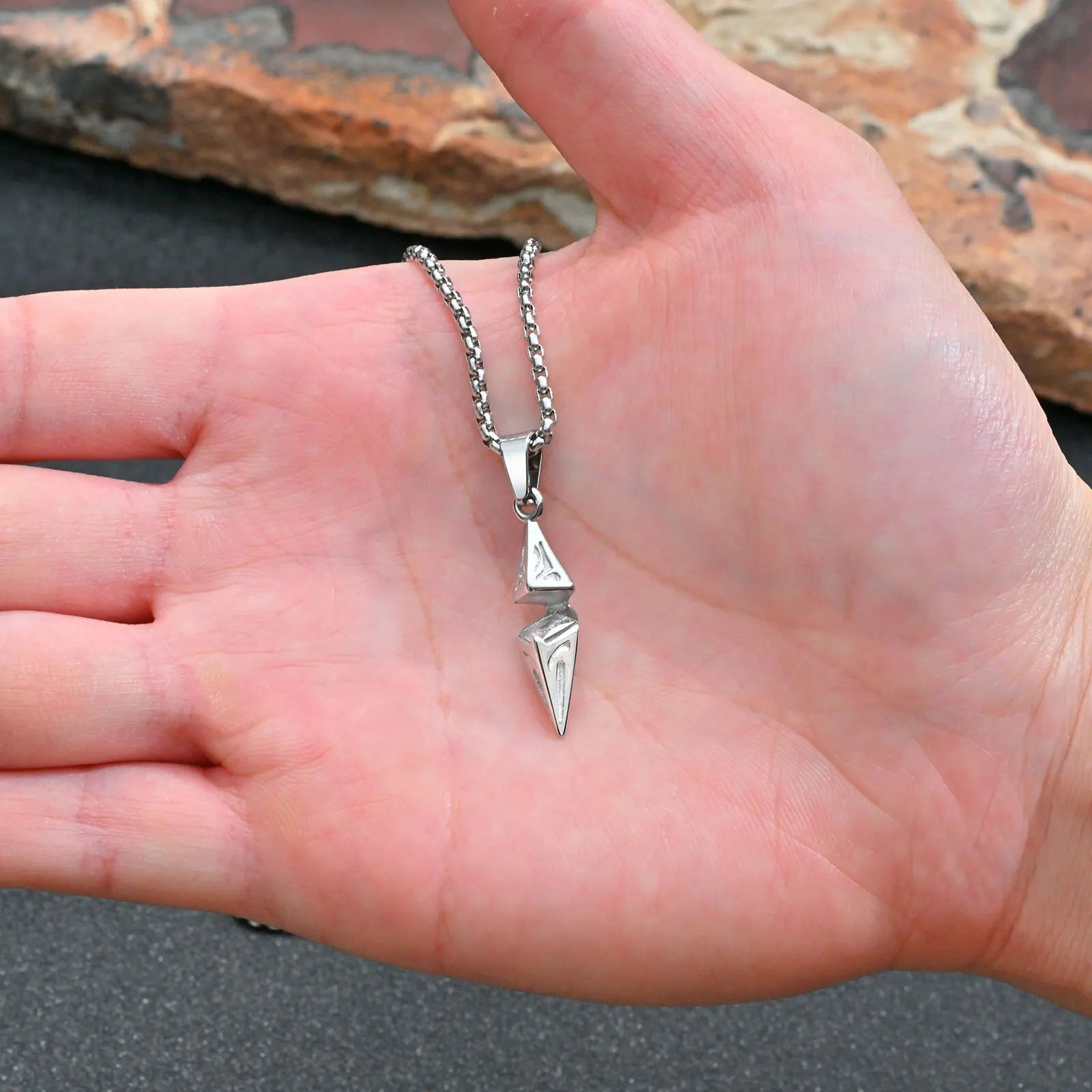 Silver arrow pendant necklace held in palm showing compact size on box chain