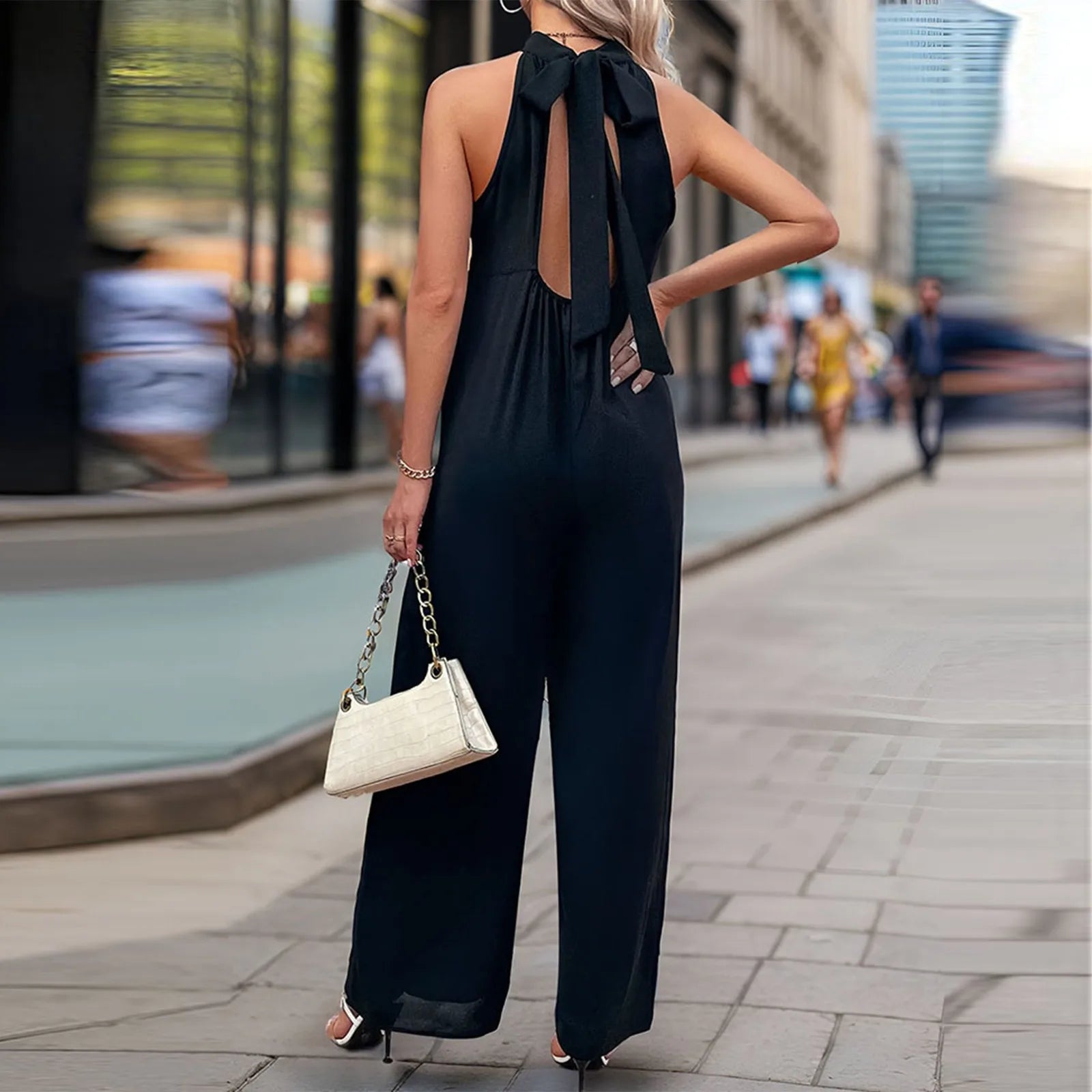 Woman wearing a wide-leg sleeveless jumpsuit in black with bow-tie back.